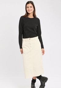 Un haut noir à manches longues associé à une jupe en velours côtelé crème de longueur genou avec une poche avant et une fermeture à bouton, portée avec des bottines noires.