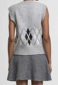 Femme portant un gilet en maille gris sans manches avec un motif argyle noir et blanc, associé à une mini-jupe grise côtelée.