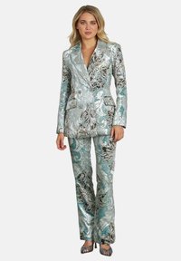 Metaalachtige turquoise pak met complexe zwart en zilver bloemenpatronen. Dubbelzijdige blazer en bijpassende fitted broek. Geweven stof.