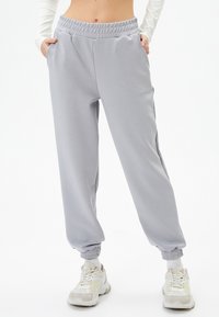 Pantalones de chándal grises claros hechos de una tela suave, con una cintura elástica, bolsillos laterales y puños acanalados en los tobillos.