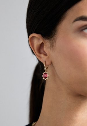 Orecchini a cerchio in oro con un grosso particolare ovale rosa circondato da piccole pietre trasparenti, appesi a un gancio in oro texturizzato.