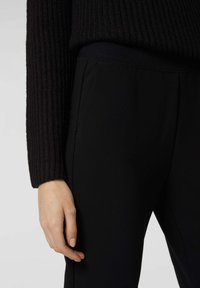 Maglione nero a costine con maniche lunghe, abbinato a pantaloni neri in tessuto morbido ed elasticizzato con tasche laterali discrete.