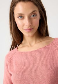 Suéter de punto rosa claro con un escote ancho y textura acanalada. Presenta mangas raglán y un acabado suave, ideal para el uso diario.