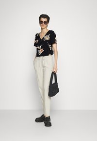 Top preto de flores de manga curta, calças beje com cordão, bolsa preta e sapatos grossos pretos, todos com uma textura suave e um design moderno.