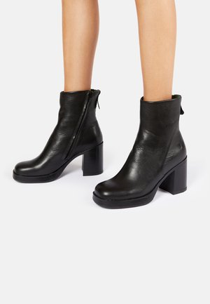 Black leather ankle boots with a block heel, featuring a side zipper and a smooth texture. The design includes a slight curved shape at the top.