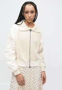 Crèmekleurige bomberjack met een textuurgebreid voorpand, gladde mouwen en een grote kraag. Voorzien van een ritssluiting en geribde boorden.
