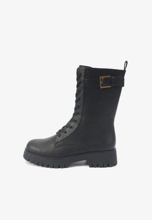 Bota de combate de cuero negro con cordones, suela de grueso perfil y correa decorativa de hebilla dorada alrededor del eje superior.