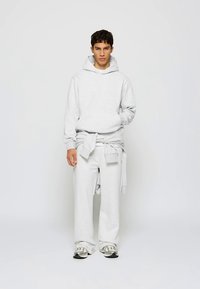 Sweat à capuche gris clair avec une poche frontale, assorti à un pantalon de survêtement large et un sweat noué à la taille. Porté avec des baskets décontractées.