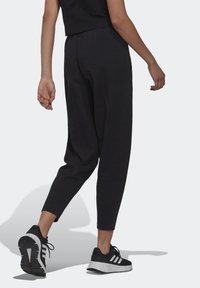 Černé zúžené joggers kalhoty vyrobené z měkké tkaniny, se splývavým pasem a staženými kotníky, doplněné černobílými sportovními botami.