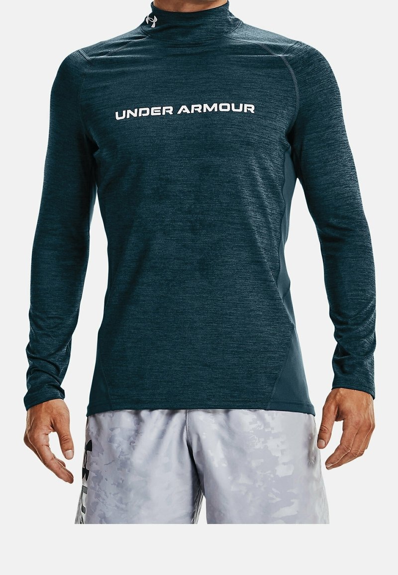 Tmavě modré sportovní tričko s dlouhými rukávy a vysokým límcem, s bílým logem "UNDER ARMOUR" na přední straně a texturovanými detaily látky.