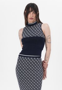 Ensemble en tricot composé d'un haut sans manches bleu marine à col montant et d'un motif géométrique blanc répétitif, associé à une jupe assortie.
