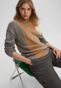 Maglione lavorato a maglia con colletto alto, caratterizzato da blocchi di colore in beige, grigio e avorio. Tessuto strutturato, con dettagli a coste sui polsini e sull'orlo.