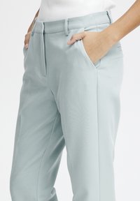 Persona vestida con pantalones ajustados de color azul claro, con las manos en los bolsillos y una blusa blanca, mostrada desde la cintura hasta la mitad del muslo.