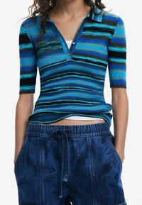 Blå randig ribbad pikétröja med krage och korta ärmar, i olika nyanser av blått, svart och grönt. Matchas med denimshorts.