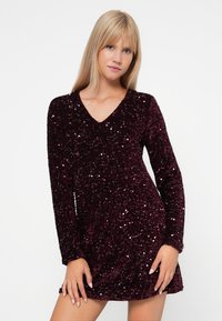 Bordový trblietavý šaty s dlhými rukávmi a výstrihom do V; priliehavý strih s textúrovaným povrchom a lesklými akcentmi po celom obvode.
