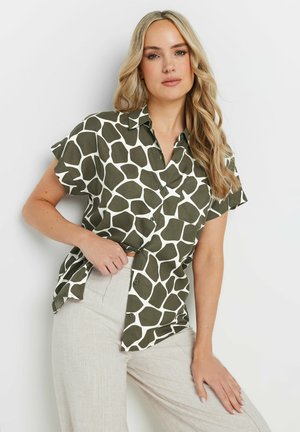 Groene kortemouwenshirt met een wit, onregelmatig geometrisch patroon. Met knopen, van lichtgewicht stof, en met kraag. Gepaard met lichtbeige broeken.