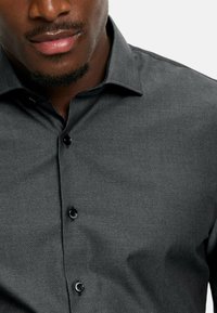 Donkergrijze button-up overhemd met een fijn textuurpatroon, een klassieke kraag en zwarte knopen. De stof lijkt glad en lichtgewicht.