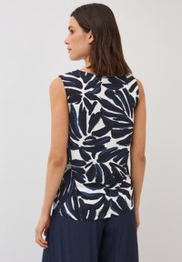 Top senza maniche bianco con un motivo foglia navy. Tessuto morbido, scollatura rotonda, orlo curvo e vestibilità rilassata, progettato per il comfort.