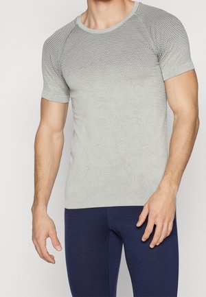 Mann trägt kurzärmeliges, grau verlaufendes, strukturiertes Sportshirt und dunkelblaue eng anliegende Leggings vor einfarbigem Hintergrund.