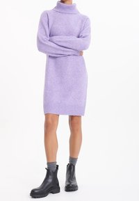 Robe en maille lavande avec un col roulé haut, des manches longues et un ourlet côtelé. Portée avec des bottines noires et des chaussettes grises.