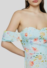 Abito floreale azzurro chiaro con design off-shoulder. Presenta maniche morbide e voluminose e un corpino aderente decorato con motivi floreali colorati.