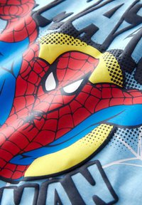 Blauer Stoff mit einem gedruckten Design, das eine rote Spider-Man-Maske zeigt, akzentuiert mit gelben und schwarzen Punkteelementen sowie fettem schwarzen Text.
