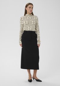 Dlhý rolákový top s dlhými rukávmi v krémovej farbe s čiernym geometrickým vzorom, skombinovaný s čiernou ceruzkovou sukňou s vysokým pásom a čiernymi lodičkami na podpätku.