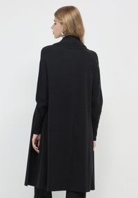 Schwarze, lange Strickjacke mit hohem Kragen und langen Ärmeln. Aus weichem Stoff gefertigt, mit seitlichen Schlitzen und einer entspannten Passform. Einfaches Design.