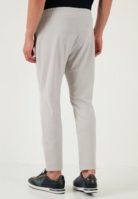 Lichtgrijze broek met een ontspannen pasvorm, elastische tailleband en achterzak. Gecombineerd met donkerblauwe sportschoenen met witte accenten.