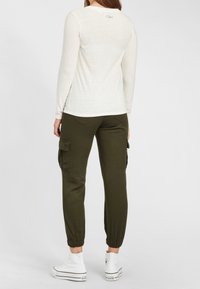 Weißes Langarmshirt mit rundem Ausschnitt, kombiniert mit olivfarbener Cargo-Hose mit Seitentaschen und elastischen Bündchen, getragen mit weißen Sneakers.