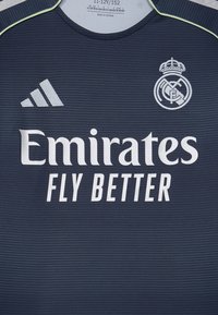 Maglietta sportiva blu scuro con texture a coste. Presenta accenti verdi, un collo rotondo, logo Adidas e la scritta "Emirates FLY BETTER" stampata in bianco.