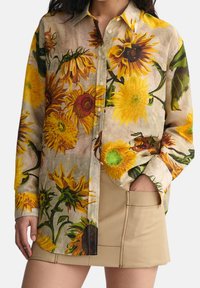 Blomstret skjorte med knaplukning, der har store gule solsikker på en lys neutral baggrund, lavet af letvægtsstof med en afslappet pasform.