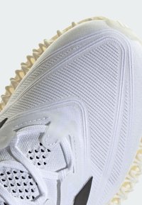 Scarpa sportiva bianca con parte superiore texture e dettagli a righe. Presenta pannelli in rete e una suola spessa con trazione. Accenti neri sui lati.