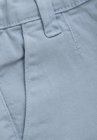 Tela de mezclilla azul claro que muestra una textura visible con detalles de costura, bolsillos y un cierre de botón en la cinturilla.