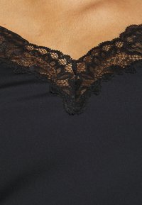Crni top s dubokim V izrezom ukrašenim složenim crnim čipkastim detaljima, koji prikazuje glatku teksturu tkanine.