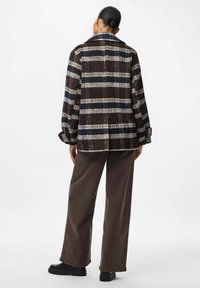 Giacca camicia a quadri marrone con colletto, grande motivo a scacchi in crema e blu navy, tessuto intrecciato e polsini abbottonati, abbinata a pantaloni larghi marroni.