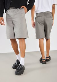 Gray shorts with a straight cut, featuring a smooth texture, side pockets, and a back pocket, paired with black shoes and white socks.