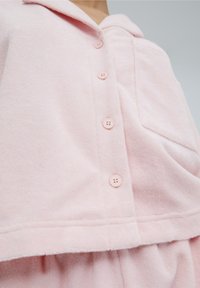 Camicetta button-up in morbido pile rosa chiaro, con colletto, sette bottoni sul davanti e una piccola tasca a sinistra.