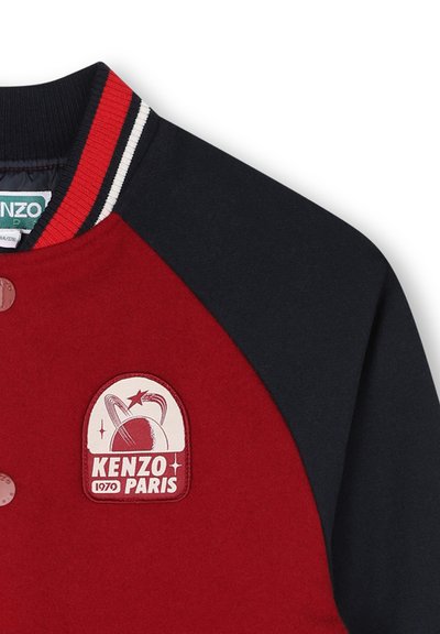 Bomber rouge et marine avec un logo brodé "KENZO PARIS" en forme ronde, col côtelé avec des rayures rouges et blanches, et boutons-pression.
