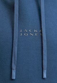 Tejido azul oscuro con dos cuerdas y el texto del logotipo en relieve "JACK & JONES" centrado entre ellas.