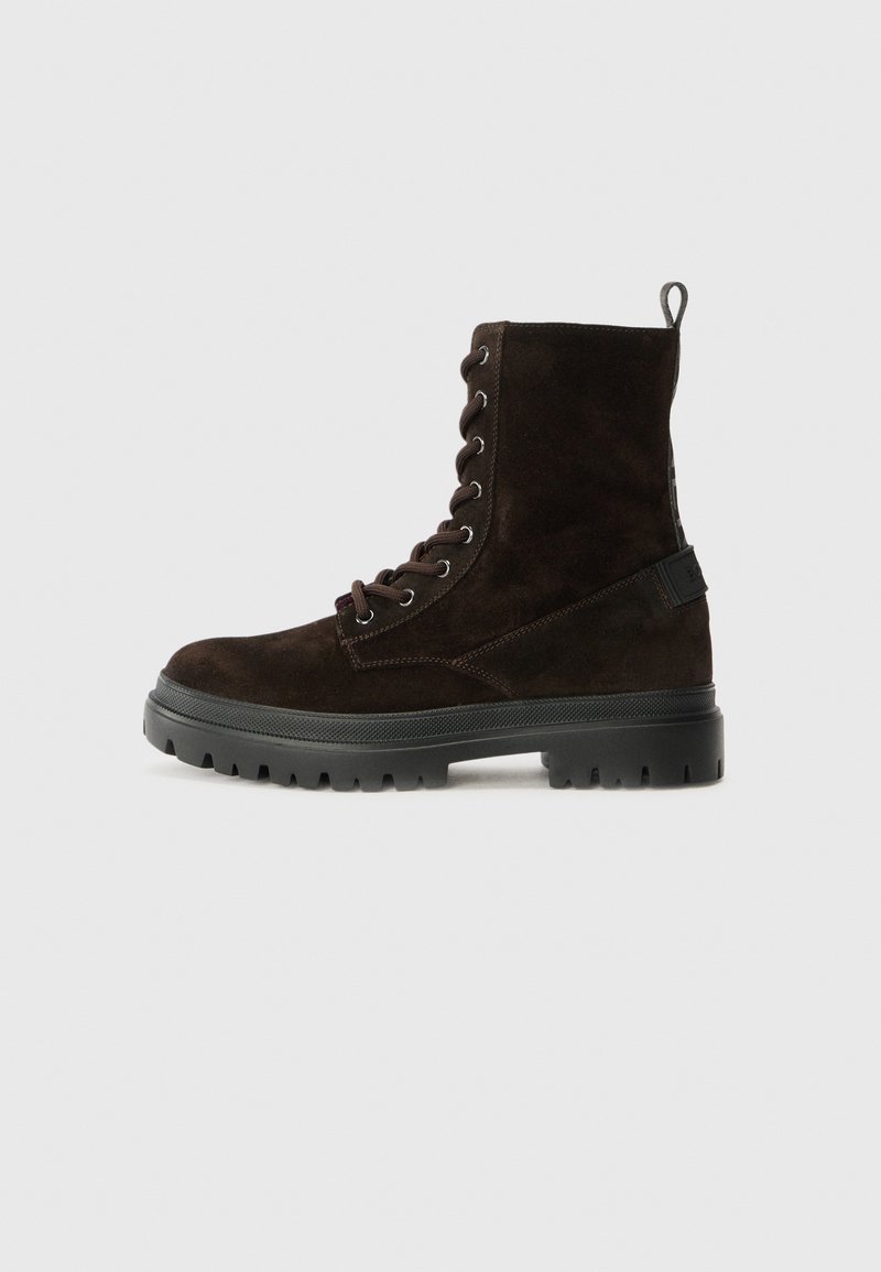 Dunkelbraune Wildleder-Schnürkampfstiefel mit dicker schwarzer Gummisohle und Zugschlaufe hinten, seitlich auf weißem Hintergrund abgebildet.