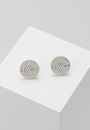 Boucles d'oreilles clous rondes en argent avec cristaux clairs regroupés au centre, gravées "Michael Kors" sur les bords, présentées sur une surface blanche.