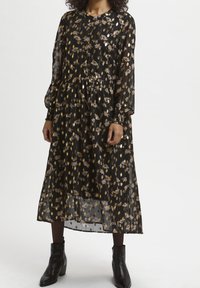 Abito nero floreale con maniche lunghe, vita arricciata e sovrapposizione trasparente. Presenta dettagli dorati e una silhouette rilassata e fluida.