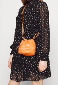 Gewebte orange Leder-Eimer-Tasche mit einem Zugverschluss und passenden Schulterriemen. Glatte Oberfläche und runde Form.