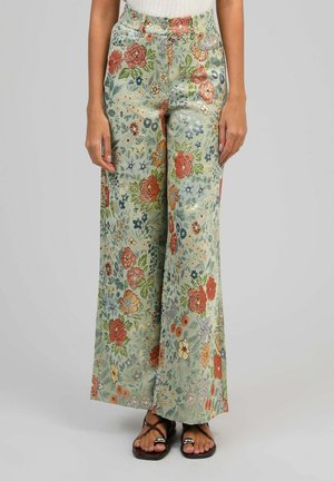 Pantalon à jambes larges avec motif floral coloré, taille haute, fermeture à boutons, porté avec des sandales noires à brides.
