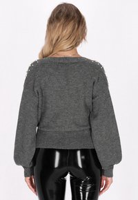 Pulover gri tricotat cu mâneci balon, tiv ciuruit și embellishmente asemănătoare perlelor pe umeri. Textură moale, design casual.