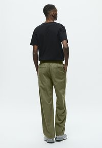 Schwarzes Baumwoll-T-Shirt mit lässigem Schnitt, kombiniert mit olivgrünen, locker sitzenden Hosen, die über aufgesetzte Taschen und eine glatte Textur verfügen.