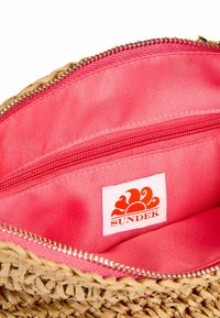Borsa in paglia intrecciata con una vivace fodera interna rosa, dotata di chiusura a zip e di una piccola etichetta logo cucita all'interno.