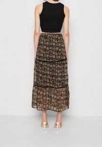 Schwarzes Crop-Top kombiniert mit einem gestuften Maxirock, der ein mehrfarbigesDiamantmuster und durchsichtige Stoffe aufweist, akzentuiert mit schwarzem Saum.