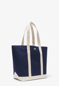 Sac cabas en toile bleu marine avec des anses crème, design carré, doté d'un petit logo vert sur le devant et d'une base crème unie.